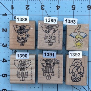 May include: A collection of six wooden stamps featuring angel designs. Each stamp has a unique angel illustration, with details like wings, hearts, and stars. The stamps are labeled with numbers and the text "STAMPIN' UP! 1995".