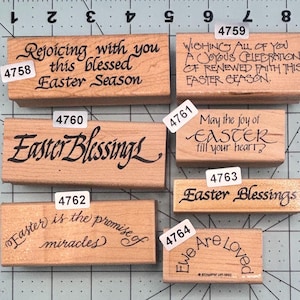 May include: A collection of wooden stamps with various Easter-themed messages in black ink. The stamps include phrases like "Easter Blessings," "Rejoicing with you," and "Easter is the promise of miracles." The stamps are rectangular and vary in size.