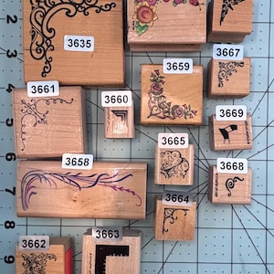 May include: A collection of wooden stamps with various decorative designs, including floral patterns, corner accents, and a butterfly. Each stamp has a unique design and a corresponding number label.
