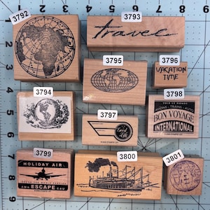 May include: A collection of wooden stamps with travel-themed designs. Includes stamps with globes, the word "Travel", a steamboat, and the phrases "Vacation Time" and "Bon Voyage International". Each stamp has a unique design.