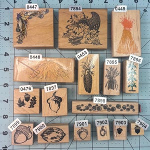 May include: A collection of wooden stamps with various fall-themed designs. The stamps feature images of cornucopias, wheat, acorns, and other autumn elements. The stamps are arranged on a grid with numbers and measurements.