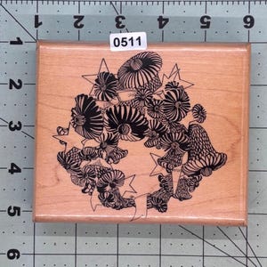 May include: A wooden stamp featuring a detailed black and white floral wreath design with star accents. The stamp has a rectangular shape and includes the number "0511" on a small white label.