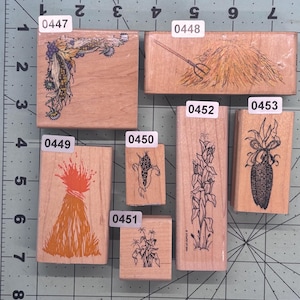 May include: A collection of wooden stamps featuring harvest-themed designs. The stamps include images of corn, wheat, and a pitchfork. The stamps are labeled with numbers and are arranged on a green cutting mat.