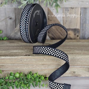 May include: A roll of black and white chequered ribbon with a length of ribbon unrolled. The ribbon is on a wooden surface with greenery in the background. The text "Exquisite Designs Hand Crafted" is visible.