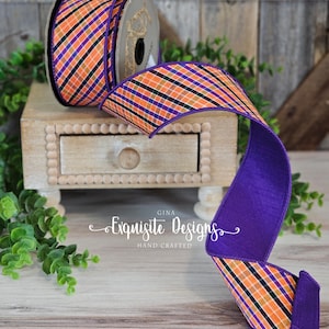 Op de afbeelding: Een rol decoratief lint met een ruitpatroon in oranje, paars, zwart en groen. Het lint wordt gepresenteerd op een kleine houten kist. De tekst "Exquisite Designs Hand Crafted" is zichtbaar.
