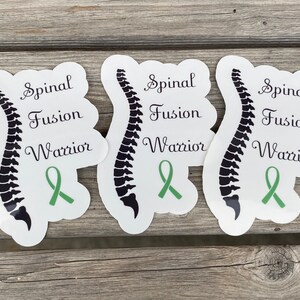 May include: Three white stickers with a black spine illustration, green ribbon, and the text "Spinal Fusion Warrior".