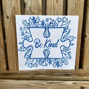 May include: Blue vinyl decal with a puzzle piece design and the words "Be Kind" surrounded by a floral border.
