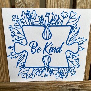 May include: Blue puzzle piece with the words "Be Kind" inside, surrounded by a floral design.