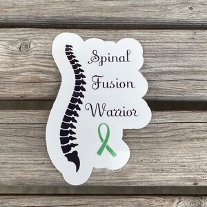 May include: White sticker with a black silhouette of a spine and the text "Spinal Fusion Warrior" with a green ribbon.