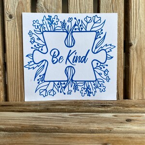 May include: Blue puzzle piece with the words "Be Kind" surrounded by a border of blue flowers and leaves on a white background.