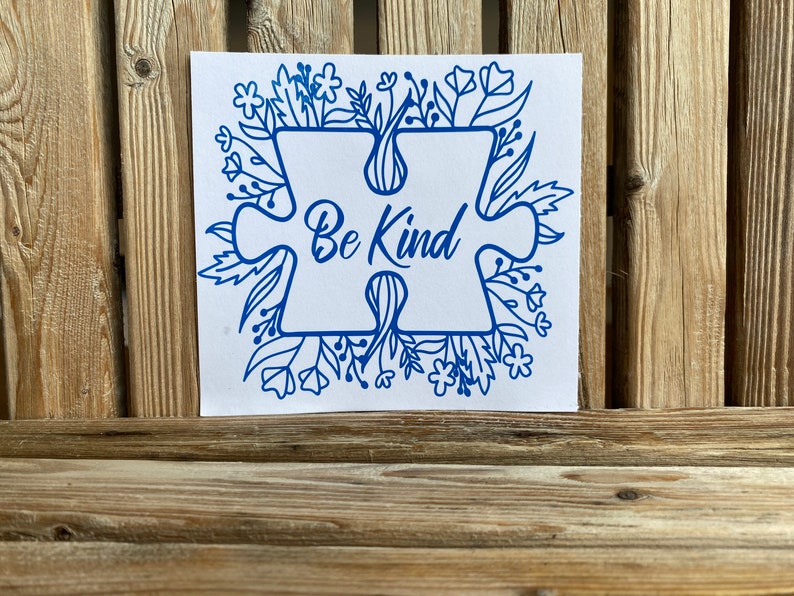May include: Blue puzzle piece with the words "Be Kind" surrounded by a border of blue flowers and leaves on a white background.