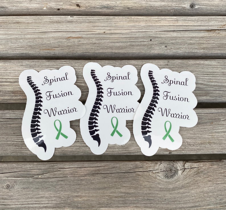 May include: Three white stickers with a black spinal column illustration and green ribbon. The text on each sticker reads "Spinal Fusion Warrior".