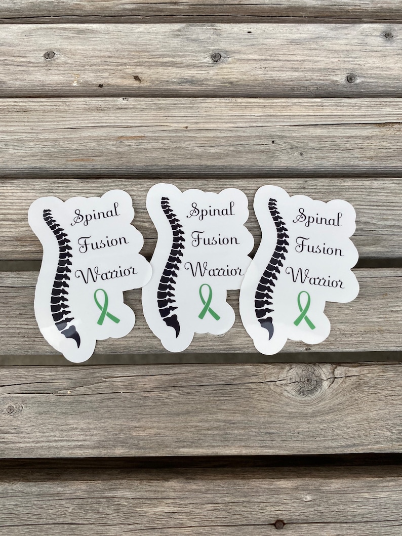 May include: Three white stickers with a black spinal column illustration and green ribbon. The text on the stickers reads "Spinal Fusion Warrior".