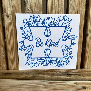 May include: Blue puzzle piece with the words "Be Kind" surrounded by a border of blue flowers and leaves on a white background.