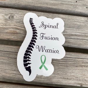 May include: White sticker with a black silhouette of a spine, the words "Spinal Fusion Warrior" and a green ribbon.