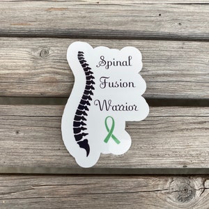 May include: White sticker with a black silhouette of a spine and the text "Spinal Fusion Warrior". A green ribbon is below the text.