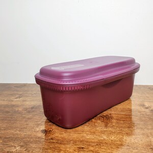 May include: A rectangular, plum-colored food storage container with a matching lid. The lid has a ridged design and a small, rectangular label. The container is made of durable plastic and is designed for food storage.