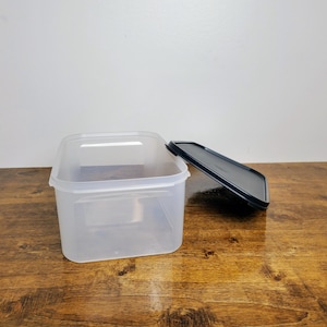 May include: A clear plastic rectangular storage container with a black lid. The lid is slightly ajar.