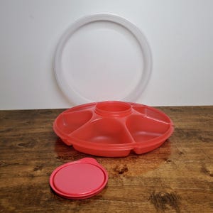 May include: A red plastic serving tray with five compartments and a clear lid. The tray has a smaller lid that fits in the center.