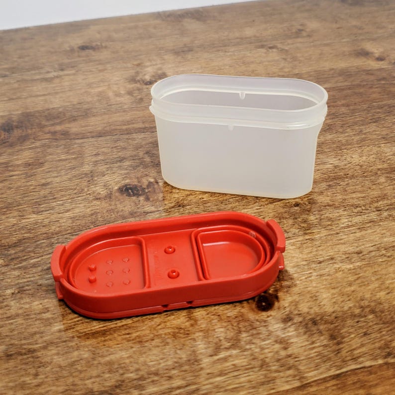 Pu&ograve; includere: Un contenitore per spezie in plastica rossa con un coperchio in plastica trasparente. Il contenitore ha un piccolo scomparto per riporre le spezie.