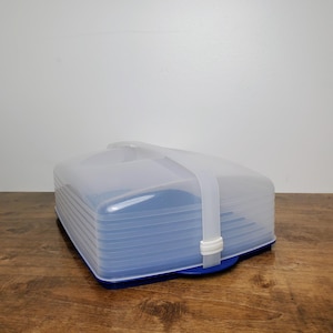 May include: A rectangular food storage container with a deep blue base and a translucent, ribbed plastic lid. The lid is secured by a white plastic strap that wraps over the top, featuring a locking mechanism on the side to keep the cover in place.