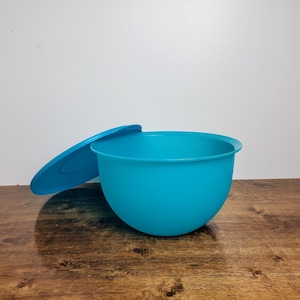 May include: A turquoise blue plastic mixing bowl with a matching lid. The bowl is sitting on a wooden surface.