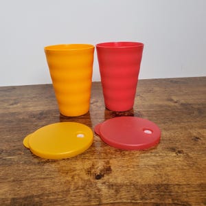 May include: Two plastic cups with lids, one yellow and one red. The cups have a wavy design and the lids have a small hole for a straw.