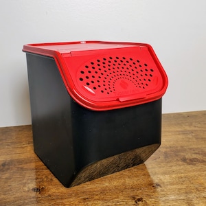 May include: A black plastic container with a red lid. The lid has a small vent with holes and the text "Tupperware" printed on it.