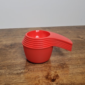 May include: A set of five red plastic measuring cups with handles. The cups are stacked on top of each other.