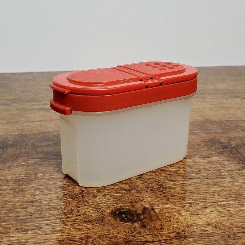Pu&ograve; includere: Un contenitore per spezie in plastica trasparente con un coperchio rosso e un tappo shaker. Il coperchio ha una piccola apertura per distribuire le spezie.