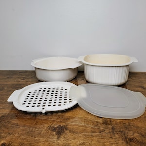 May include: White plastic steamer set with two bowls, a lid, and a colander insert. The bowls have a ribbed design and the lid is clear.