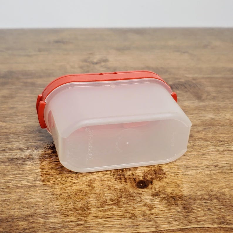 Pu&ograve; includere: Un contenitore di plastica trasparente con un coperchio rosso. Il contenitore &egrave; rettangolare con bordi arrotondati. Il coperchio ha un leggero bordo attorno al bordo.