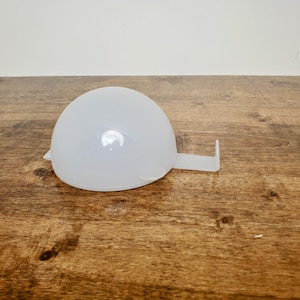 May include: A translucent white plastic measuring cup with a semi-spherical bowl and a rectangular handle. The cup is sitting on a wooden surface.