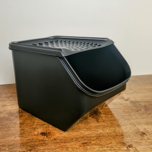 May include: A black plastic container with a hinged lid and a slotted opening. The container is designed for storing and dispensing dry goods.