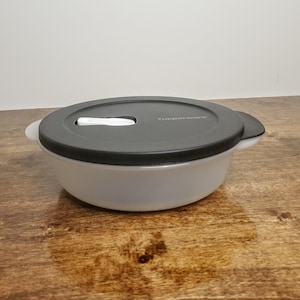 May include: A clear plastic bowl with a black lid. The lid has a white latch and the words "Tupperware" printed on it.