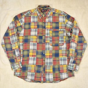 May include: A long-sleeve button-down shirt featuring a multi-colored patchwork plaid pattern in shades of red, yellow, blue, green, and white. The shirt includes a standard collar, a single chest pocket on the left side, and a full front button closure.