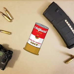 May include: An image featuring a can of soup with the text "Antifascist Action" and "For My Family Soup". The image also includes several bullets, a black magazine, and a black laser device.