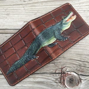 May include: A brown leather wallet with a crocodile design. The crocodile is green and has its mouth open.