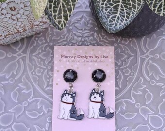 May include: A pair of dangle earrings featuring a cartoon husky dog with black and white fur. The earrings are made with surgical steel posts and backs. The card reads "Murray Designs by Lisa Handcrafted in Adelaide".