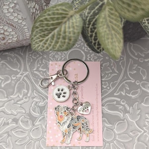 May include: A silver-colored keychain with a dog charm, paw print charm, and a heart-shaped charm that says "Best Friend". The dog charm is a colorful Australian Shepherd. The keychain is attached to a pink card with white polka dots.