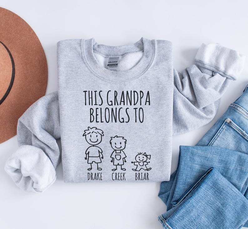 Op de afbeelding: Grijs sweatshirt met de tekst "This Grandpa Belongs To" en drie stick figuren met de namen "Drake", "Creek" en "Briar" eronder.