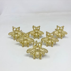 Puede incluir: Seis tiradores de cajones en forma de abeja de color dorado. El diseño de la abeja es detallado y tiene un acabado texturizado.