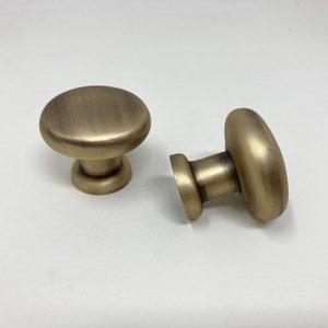 May include: Two antique gold cabinet knobs with a round, slightly domed top and a cylindrical base.