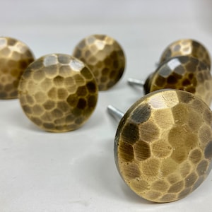 May include: Six brass cabinet knobs with a hammered finish. The knobs are round and have a slightly domed shape.