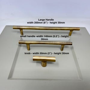 May include: Three gold cabinet hardware options: a large handle measuring 8 inches wide and 30mm high, a smaller handle measuring 5.5 inches wide and 30mm high, and a knob measuring 2 inches wide and 30mm high.