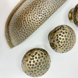 May include: A set of four antique gold cabinet knobs with a hammered finish. The knobs are round and have a textured surface.