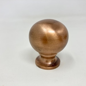 Può includere: Un pomello per armadio rotondo in rame spazzolato con una base leggermente rialzata.