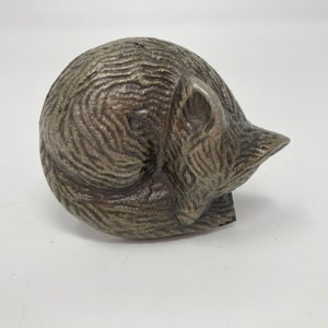 May include: A small, silver-coloured metal sculpture of a sleeping fox. The fox is curled up in a ball with its tail wrapped around its body.