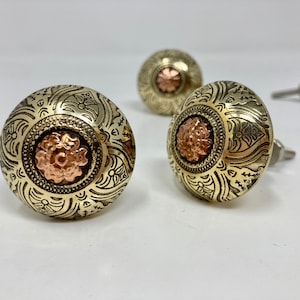 May include: Three ornate brass cabinet knobs with a copper centre. The knobs have a detailed floral design.