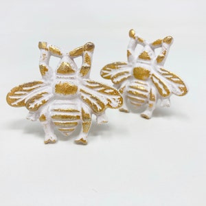 May include: Two white bee-shaped drawer pulls with gold accents. The bees have raised wings and a textured body.